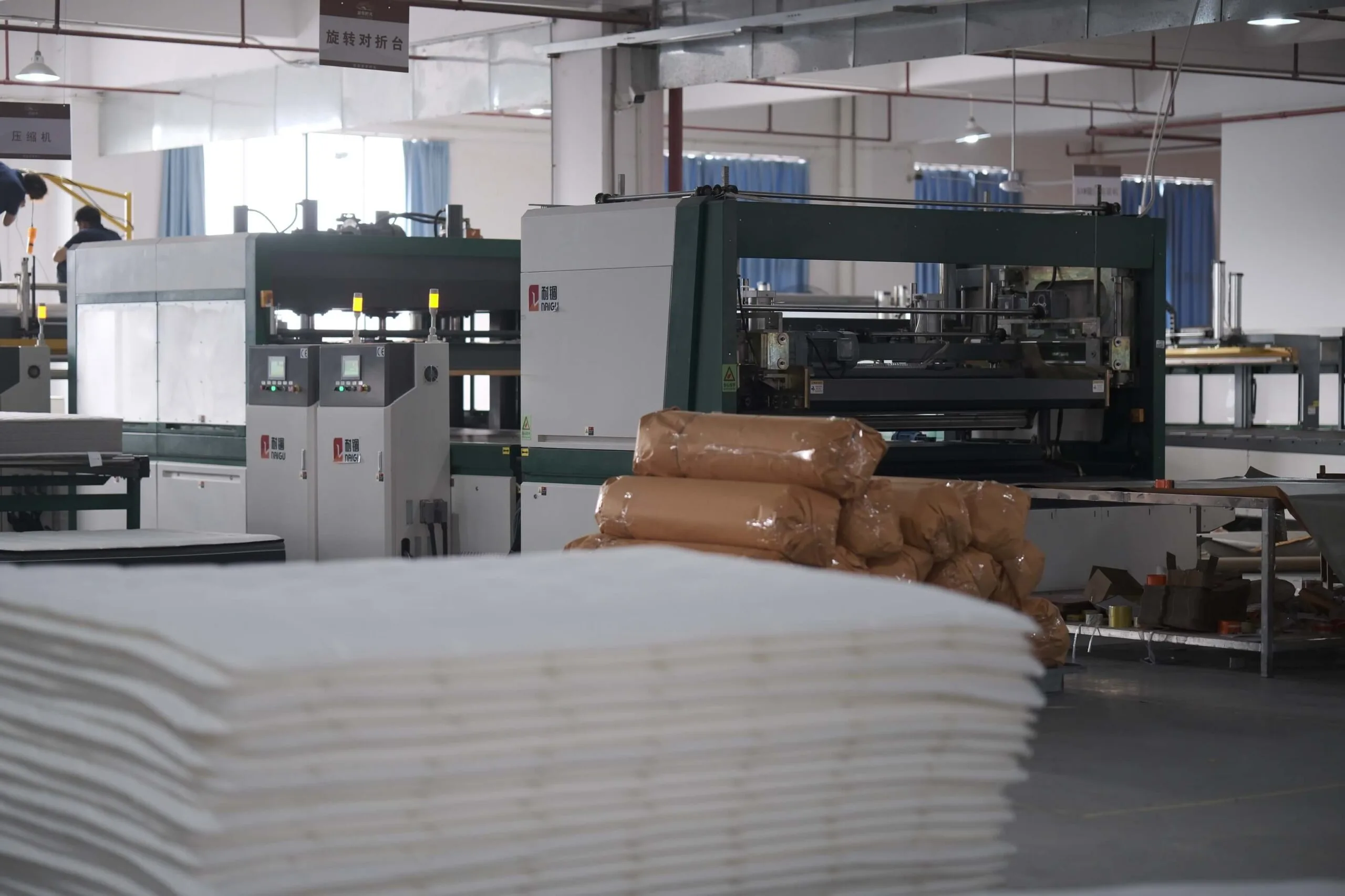 Partial view of a mattress production area showing factory machines