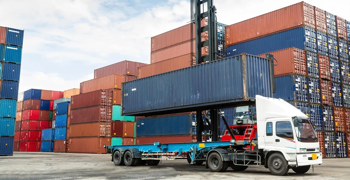 A truck loading a shipping container at a port logistics yard with stacked colorful containers