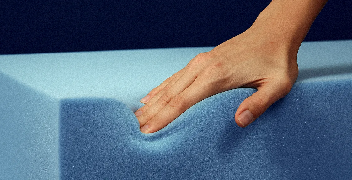 A hand pressing into blue memory foam, showing the indentation and slow rebound texture of the material
