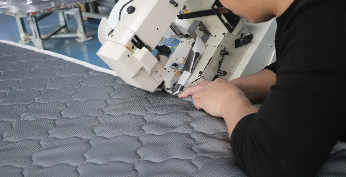 Worker quilting mattress in manufacturing plant