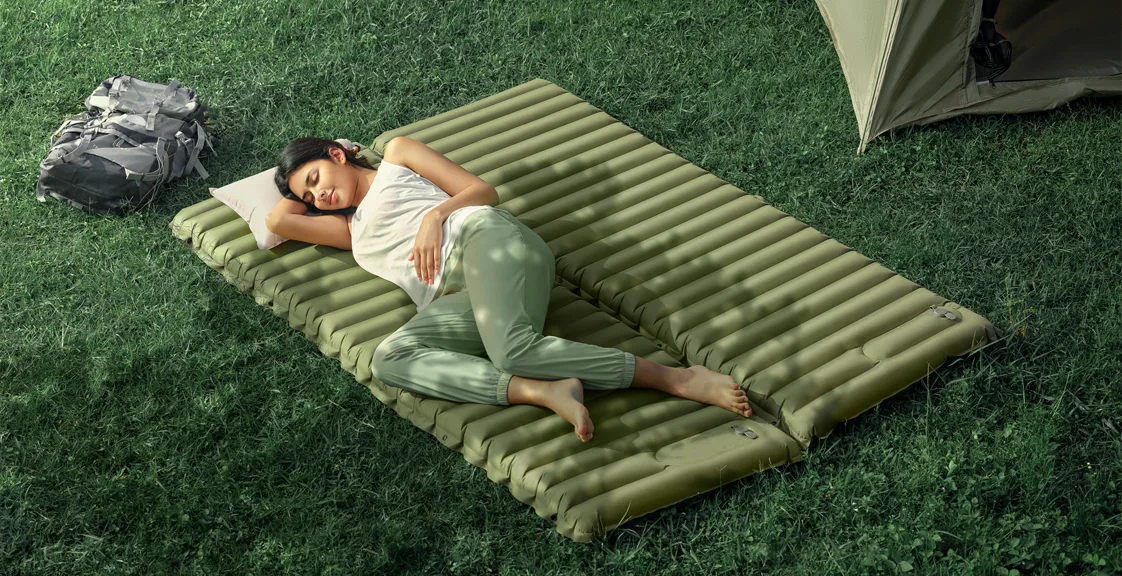Woman sleeping on an inflatable camping air mattress outdoors.
