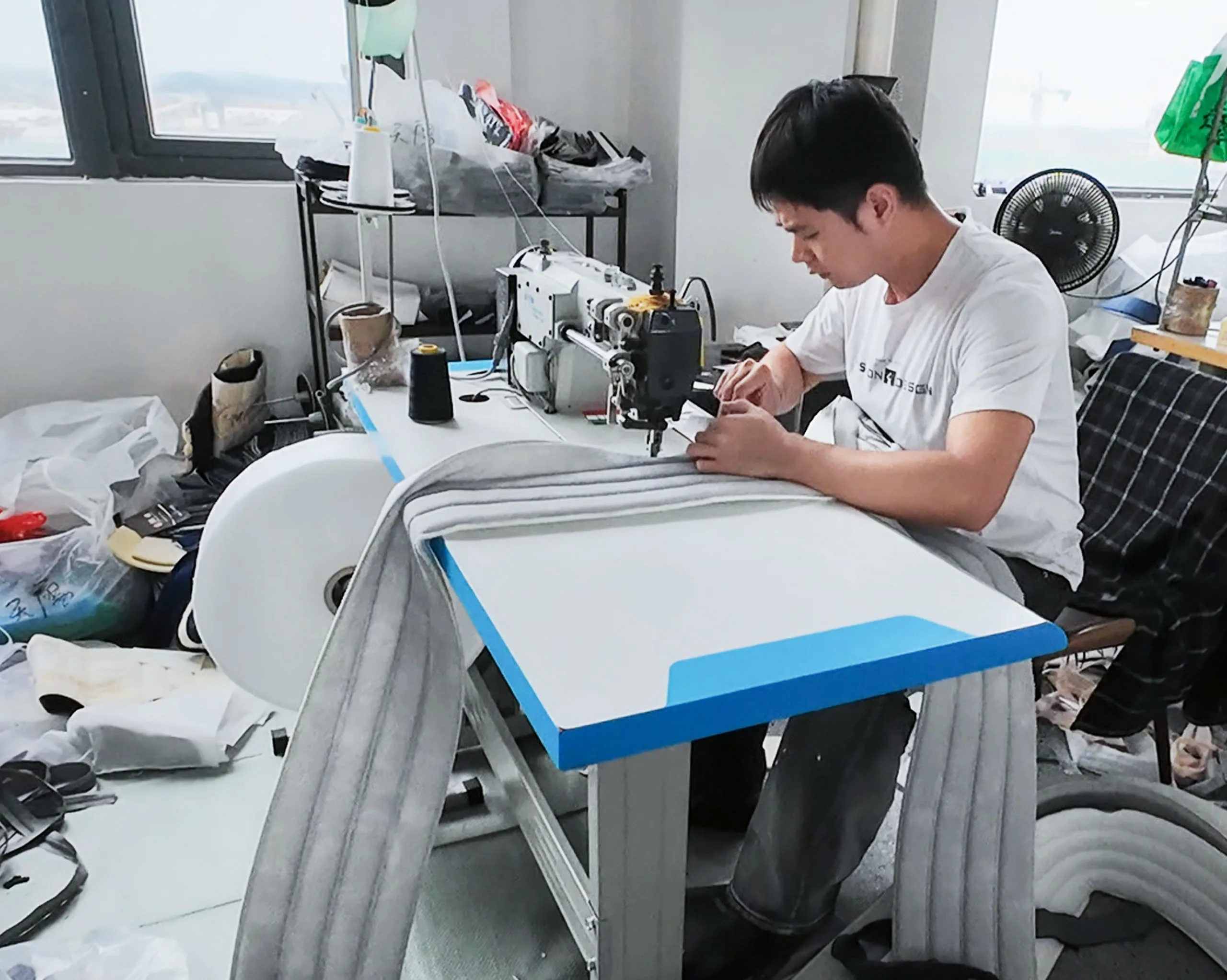 Worker sewing mattress fabric with an industrial sewing machine, showcasing detailed craftsmanship in mattress production