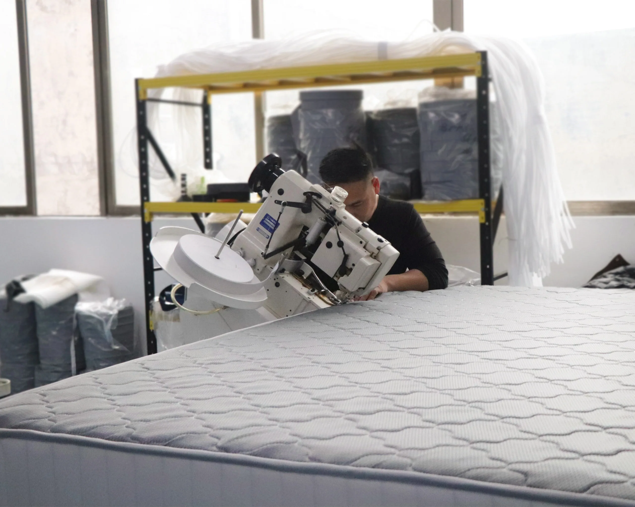 Worker using an edge binding machine to finish mattress edges, enhancing structural durability and refined appearance